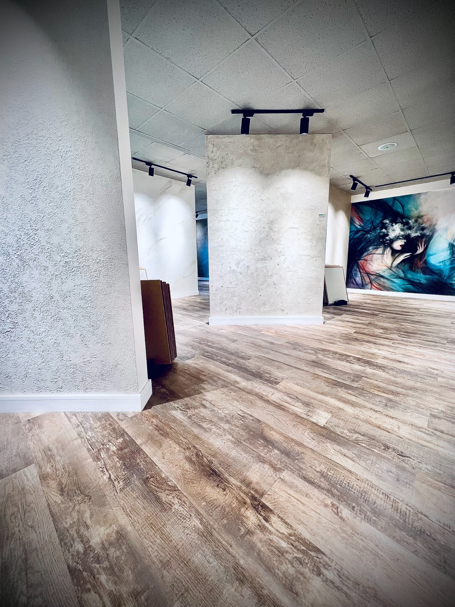 Wnętrze z dekoracyjnymi tynkami strukturalnymi na ścianach, oświetleniem punktowym na szynach i panelami podłogowymi imitującymi drewno. Widoczny fragment dużego, abstrakcyjnego obrazu na ścianie.