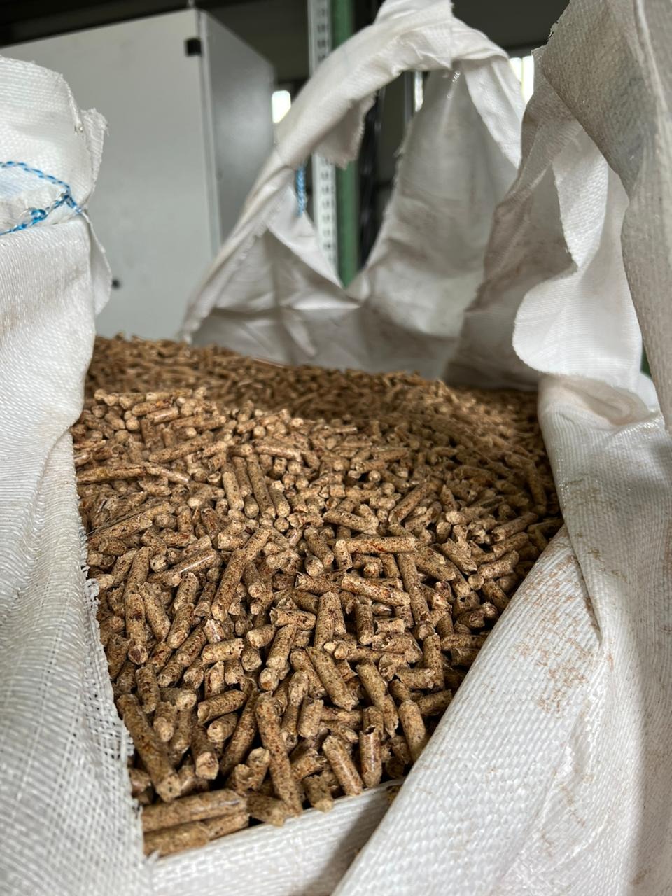 Wnętrze worka wypełnionego brązowymi, cylindrycznymi granulkami z widocznymi fragmentami drewna, na tle metalowej konstrukcji.