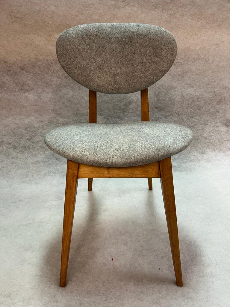 Krzesło z drewnianą ramą i tapicerowanym siedziskiem oraz oparciem w szarym kolorze, na tle szarego tła.