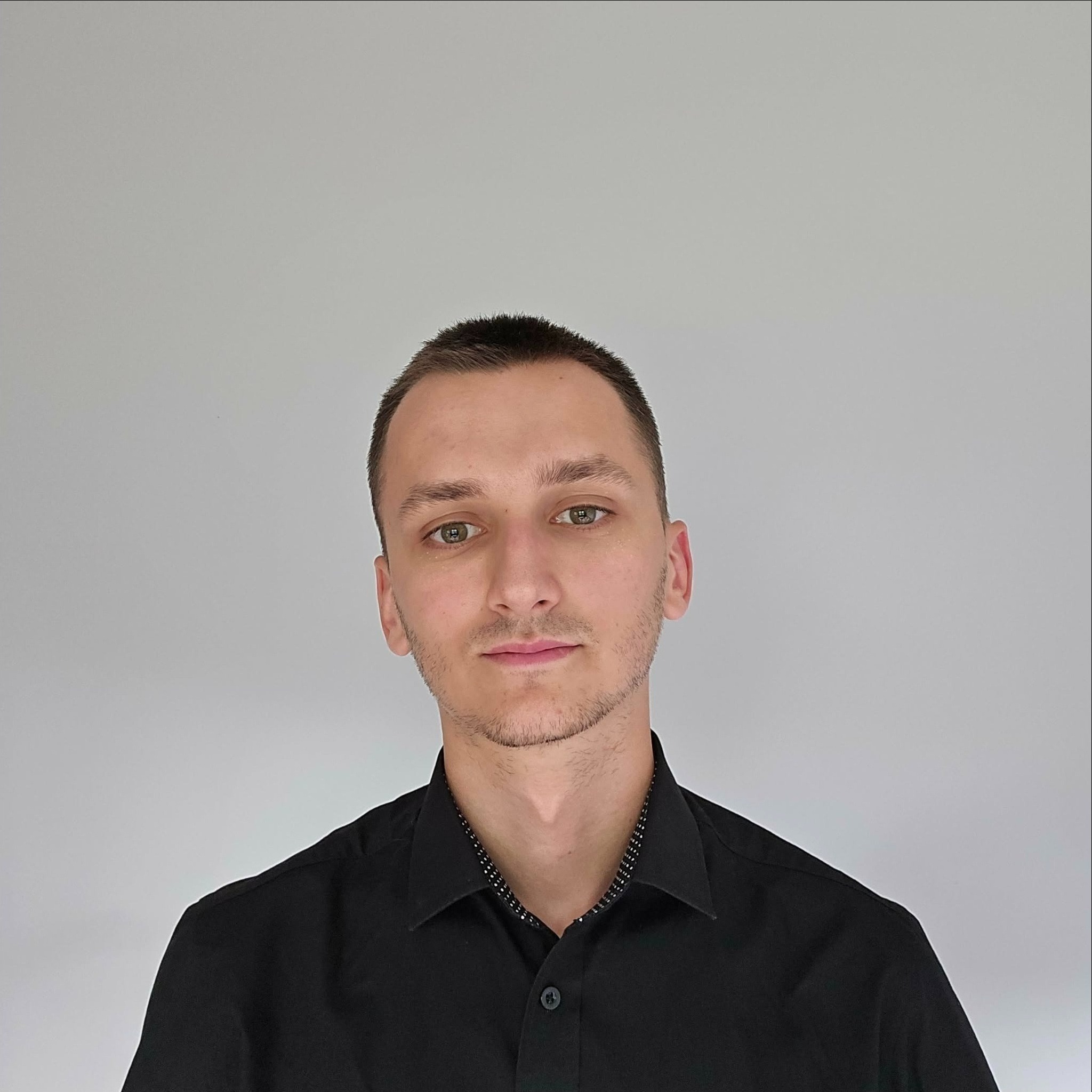 Portret młodego mężczyzny z krótkimi włosami i zielonymi oczami w czarnej koszuli, na jasnym tle. Zdjęcie profilowe z Wrocławia.