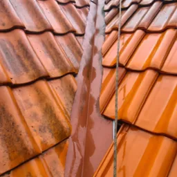 Część dachu z ceramiczną dachówką przed i po myciu, widoczna różnica w kolorze i czystości, z mokrą rynną w pionie po prawej stronie.