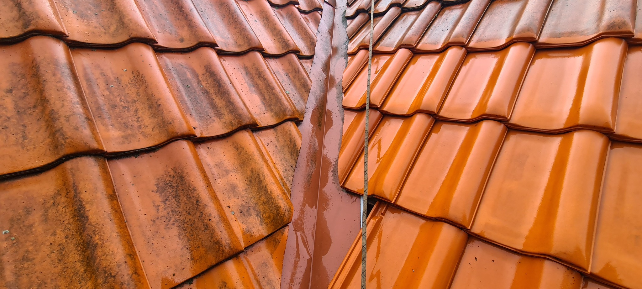 Część dachu z ceramiczną dachówką przed i po myciu, widoczna różnica w kolorze i czystości, z mokrą rynną w pionie po prawej stronie.