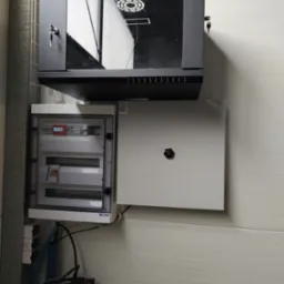 Zamknięta szafa rack LanTechnic z kluczem w zamku, pod nią otwarta skrzynka rozdzielcza z licznikiem energii elektrycznej i zamknięta skrzynka z pokrętłem na ścianie z paneli.