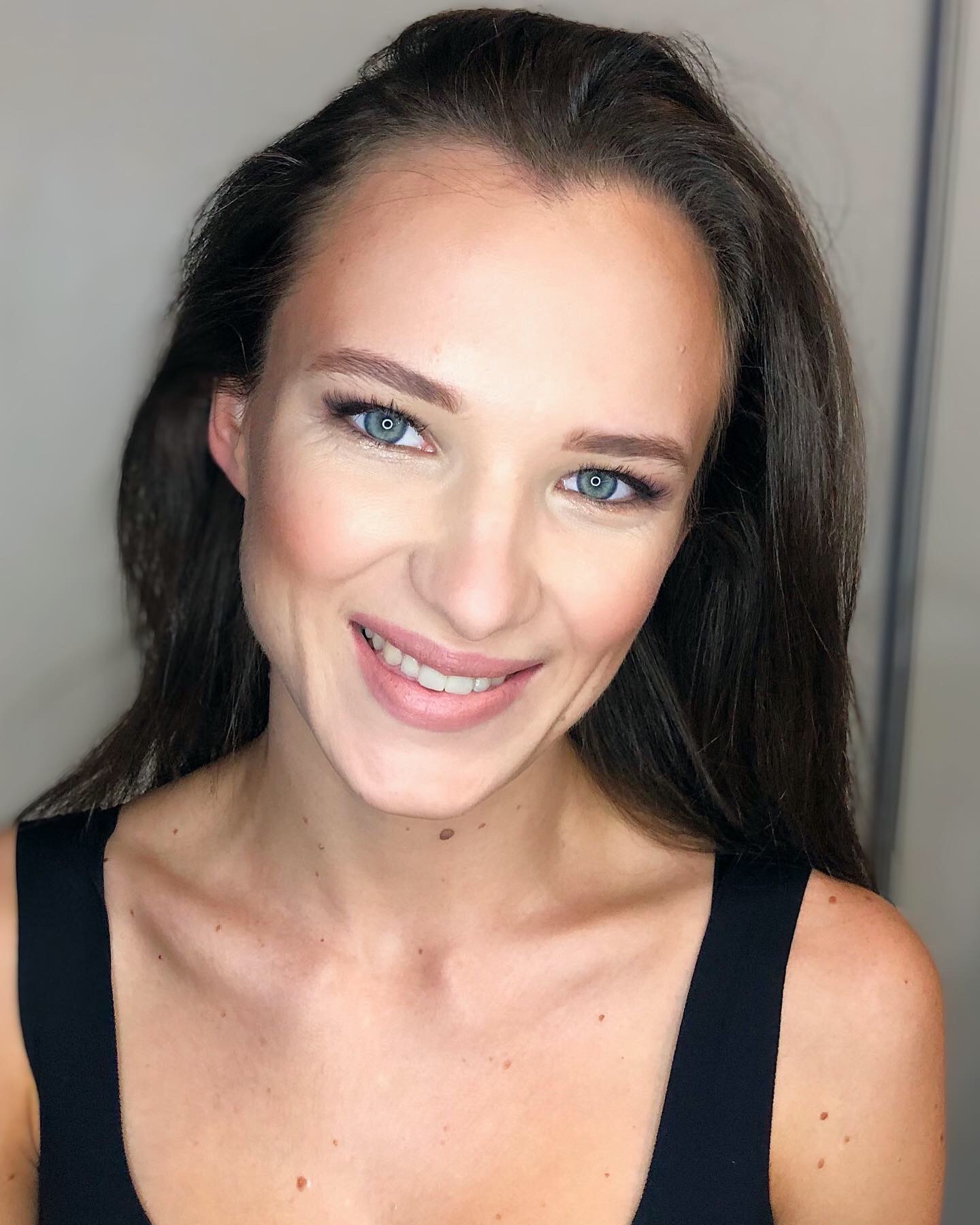 Portret kobiety z delikatnym podkreśleniem oczu i naturalnym wykończeniem cery, uwydatniającym jej niebieskie oczy.