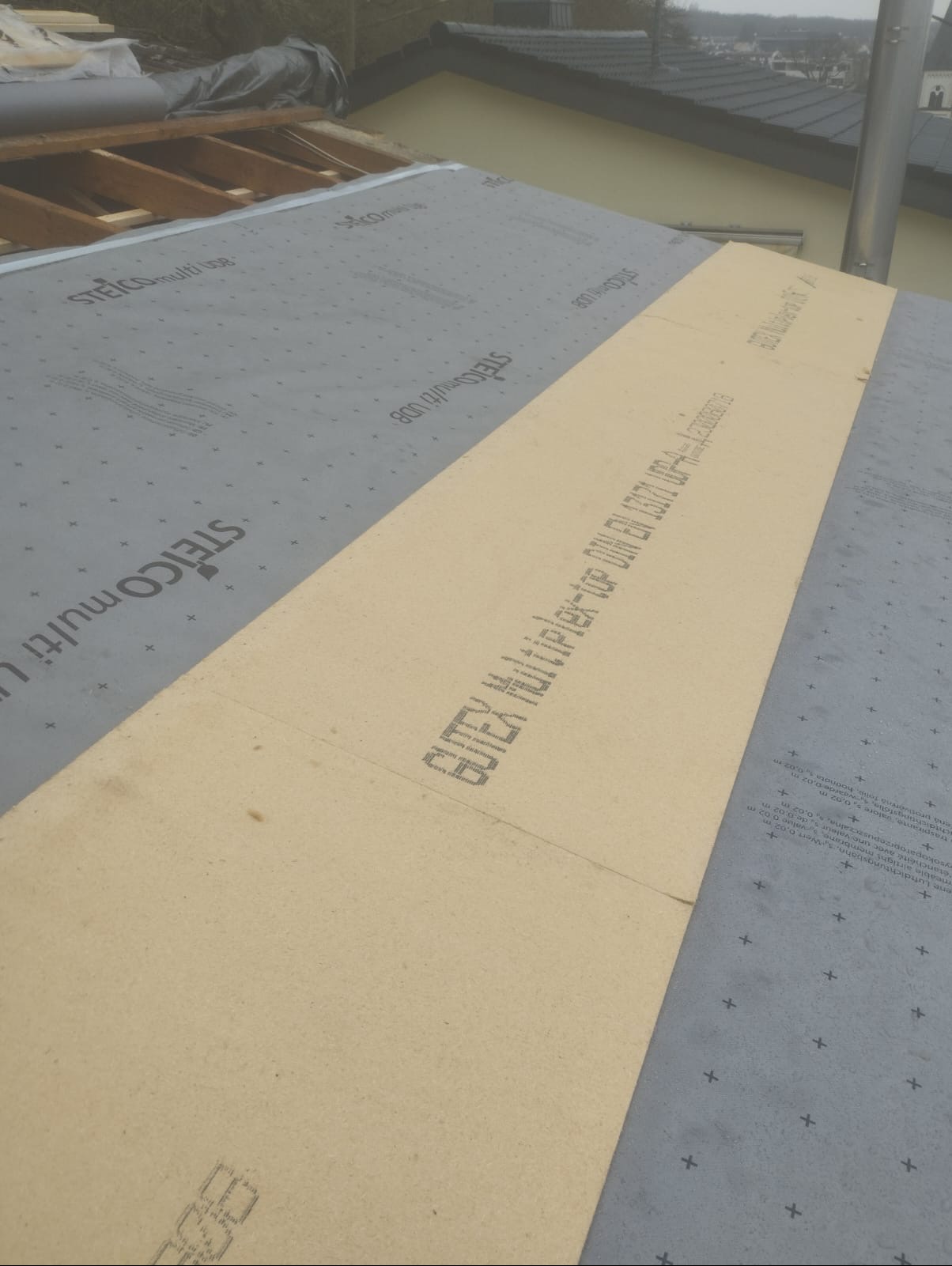 Montaż warstwy izolacyjnej z płyt GUTEX Multiplex-tape na dachu, widoczne membrany STEICO multi UDB i konstrukcja więźby dachowej.