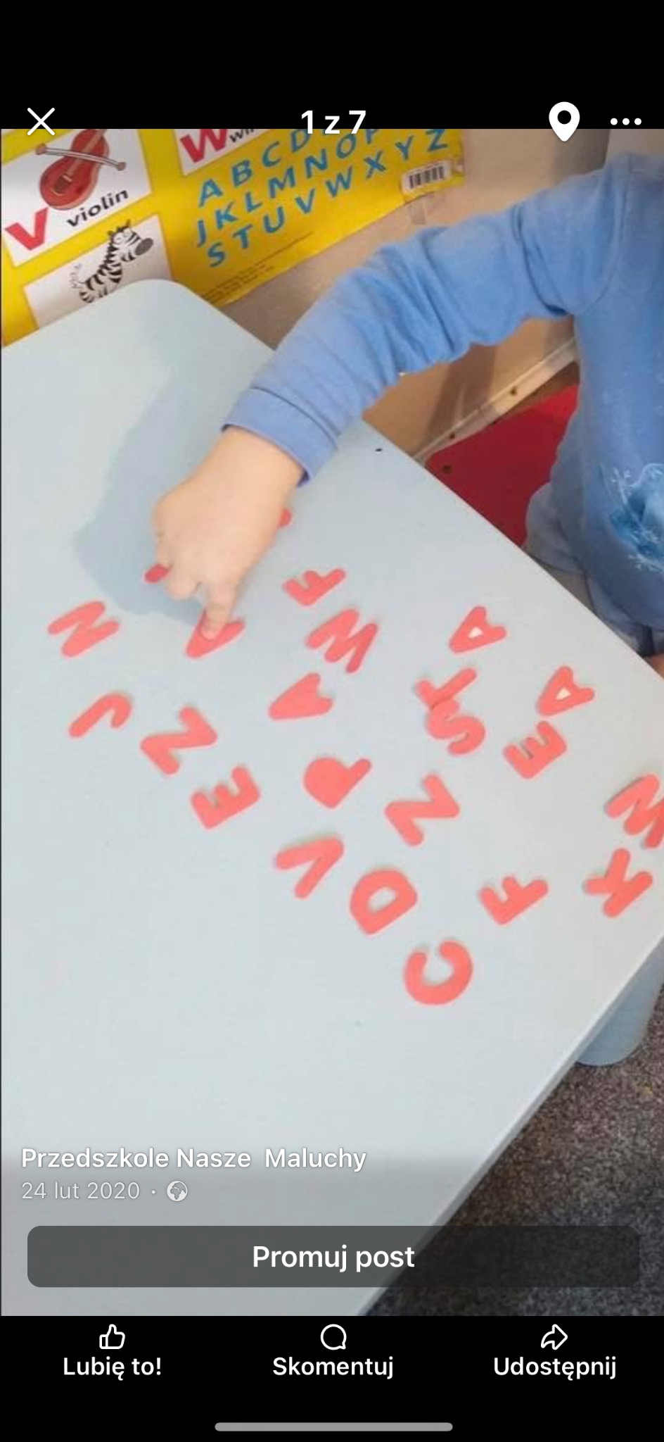 Dziecko układa litery z pianki na stole w żłobku. W tle plakat edukacyjny z alfabetem i obrazkami. Nauczanie przez zabawę, edukacja wczesnoszkolna.