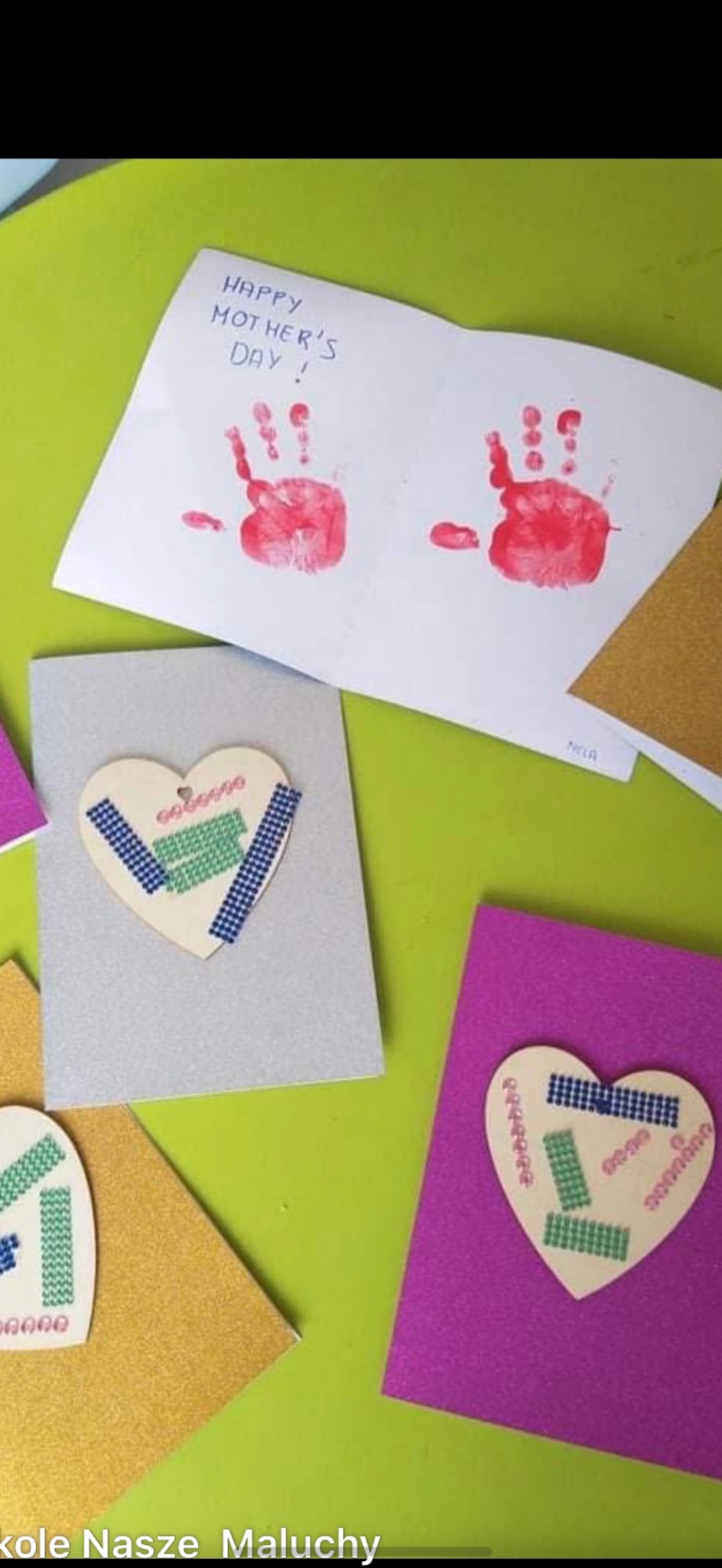 Ręcznie robione kartki na Dzień Matki z odciskami dłoni i serduszkami z taśmy washi, ułożone na zielonym stole. Kreatywne prace plastyczne dzieci.