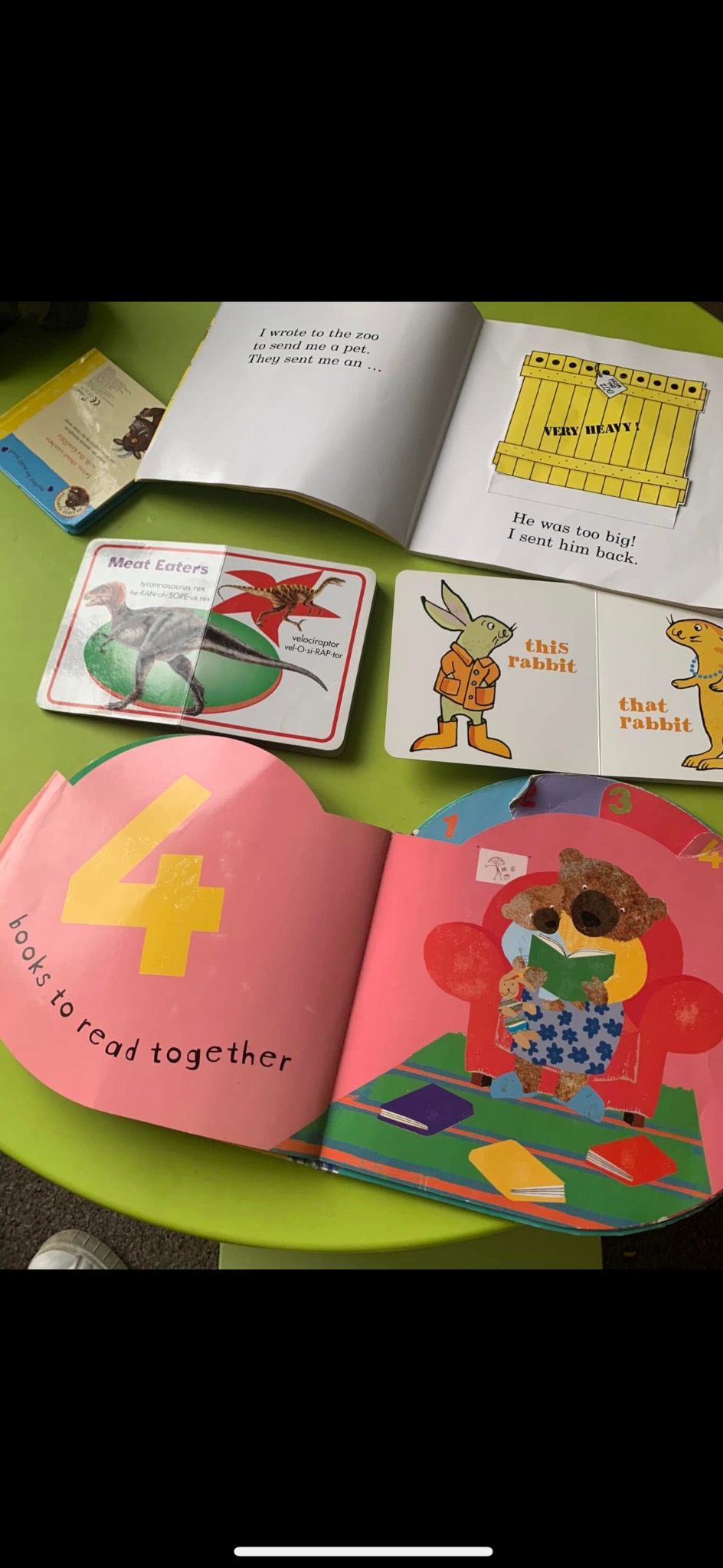 Kolorowe książeczki dla dzieci leżące na zielonym stoliku, otwarte na różnych stronach. Widoczne ilustracje zwierząt i cyfr. Edukacyjne materiały dla żłobka.