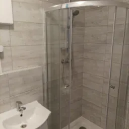 Nowoczesna łazienka z kabiną prysznicową narożną, umywalką z szafką i płytkami imitującymi drewno na ścianach.