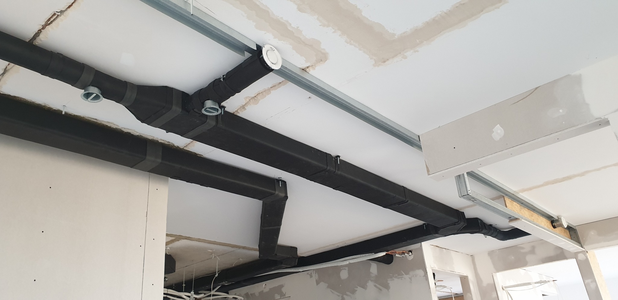 Montaż czarnych, zaizolowanych przewodów wentylacyjnych pod sufitem podwieszanym w trakcie wykończenia wnętrza, widoczne elementy mocujące i instalacja elektryczna.