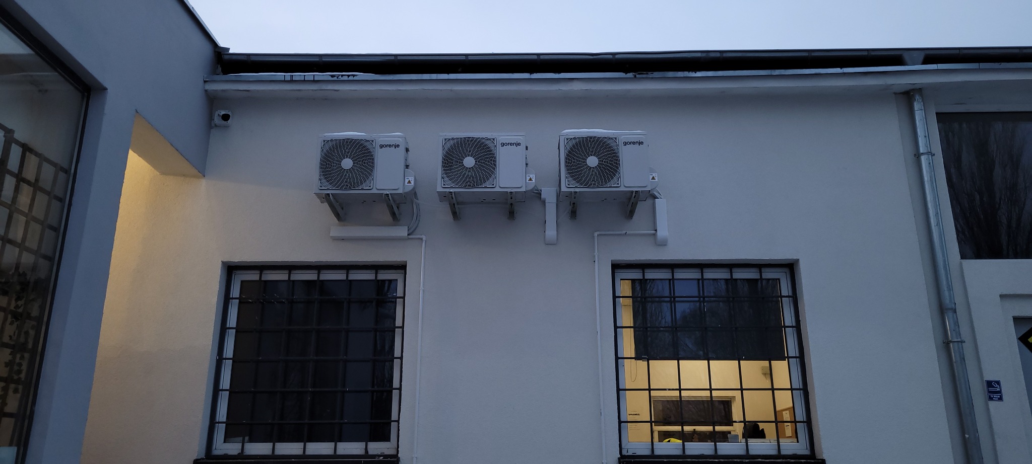 Trzy jednostki zewnętrzne klimatyzacji Gorenje zamontowane na białej ścianie budynku z widocznymi oknami z kratami.