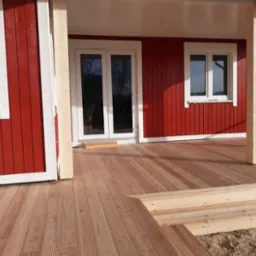 Czerwony dom szkieletowy z drewnianym tarasem i schodami, widok z niskiej perspektywy, jasne światło dzienne.