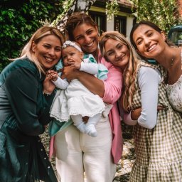 Marta Wójcik - Cztery uśmiechnięte kobiety pozują z niemowlęciem w białej sukience i opasce na głowie, na tle zieleni i białej brzozy.