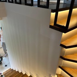 ArtSpawDesign MIODEK Marek Borowczak - Nowoczesne schody drewniane z podświetleniem LED, czarne metalowe barierki, biała ściana, widok z góry.