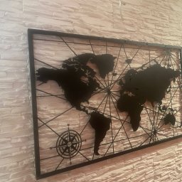 ArtSpawDesign MIODEK Marek Borowczak - Metalowa mapa świata z kompasem, zawieszona na dekoracyjnej ścianie z białej cegły.