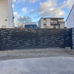 ArtSpawDesign MIODEK Marek Borowczak - Nowoczesna, przesuwna brama wjazdowa z poziomymi, prostokątnymi wycięciami, zamontowana między dwoma budynkami, z widocznym białym vanem w tle.