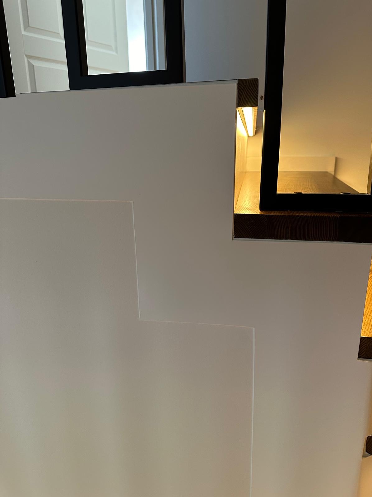 Fragment nowoczesnego, minimalistycznego ogrodzenia z białych paneli z podświetleniem LED i elementami w kolorze ciemnego drewna.