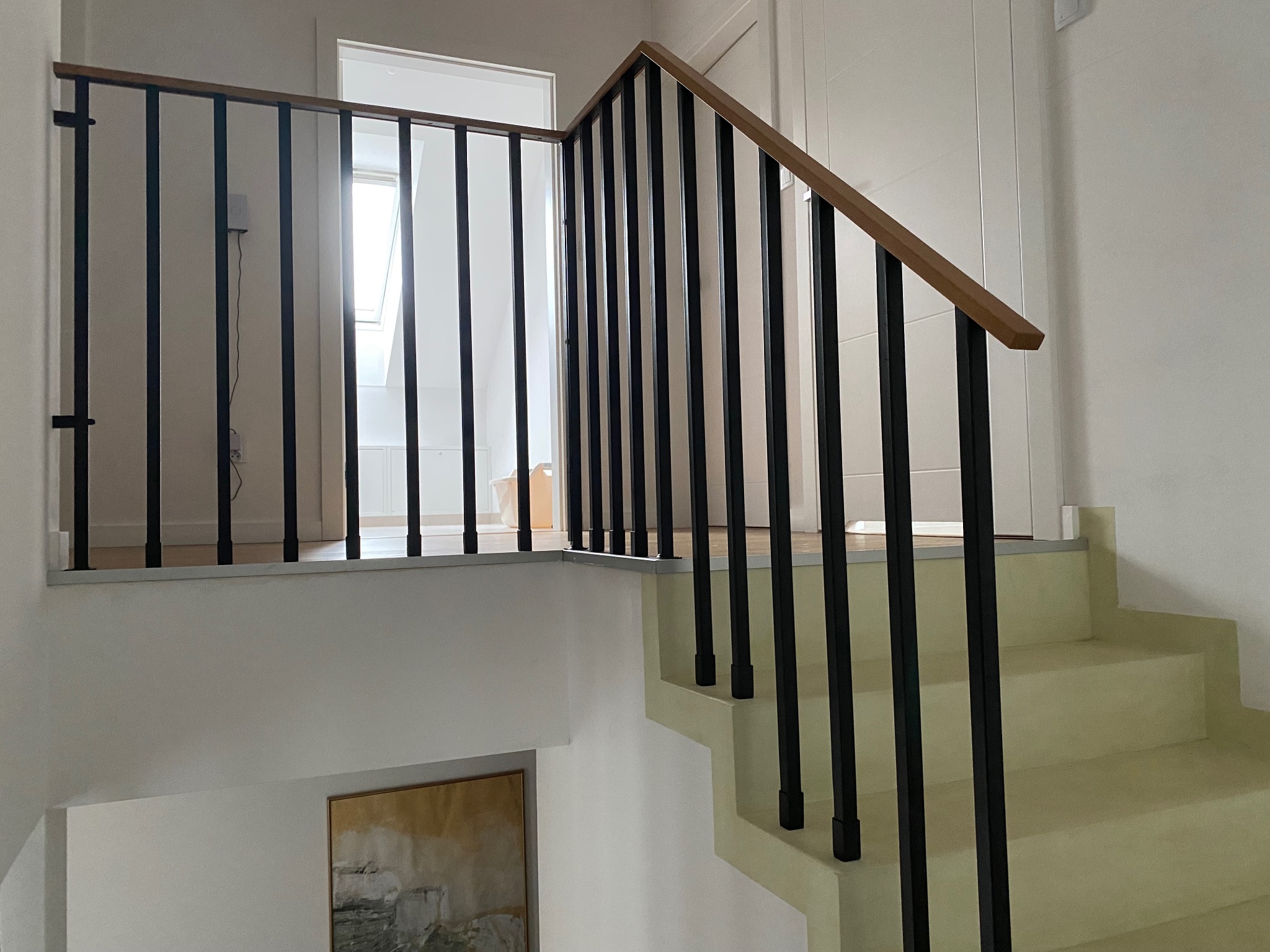 Nowoczesne schody z czarną metalową balustradą i drewnianym poręczą, widok z dołu, jasne wnętrze, minimalistyczny design.