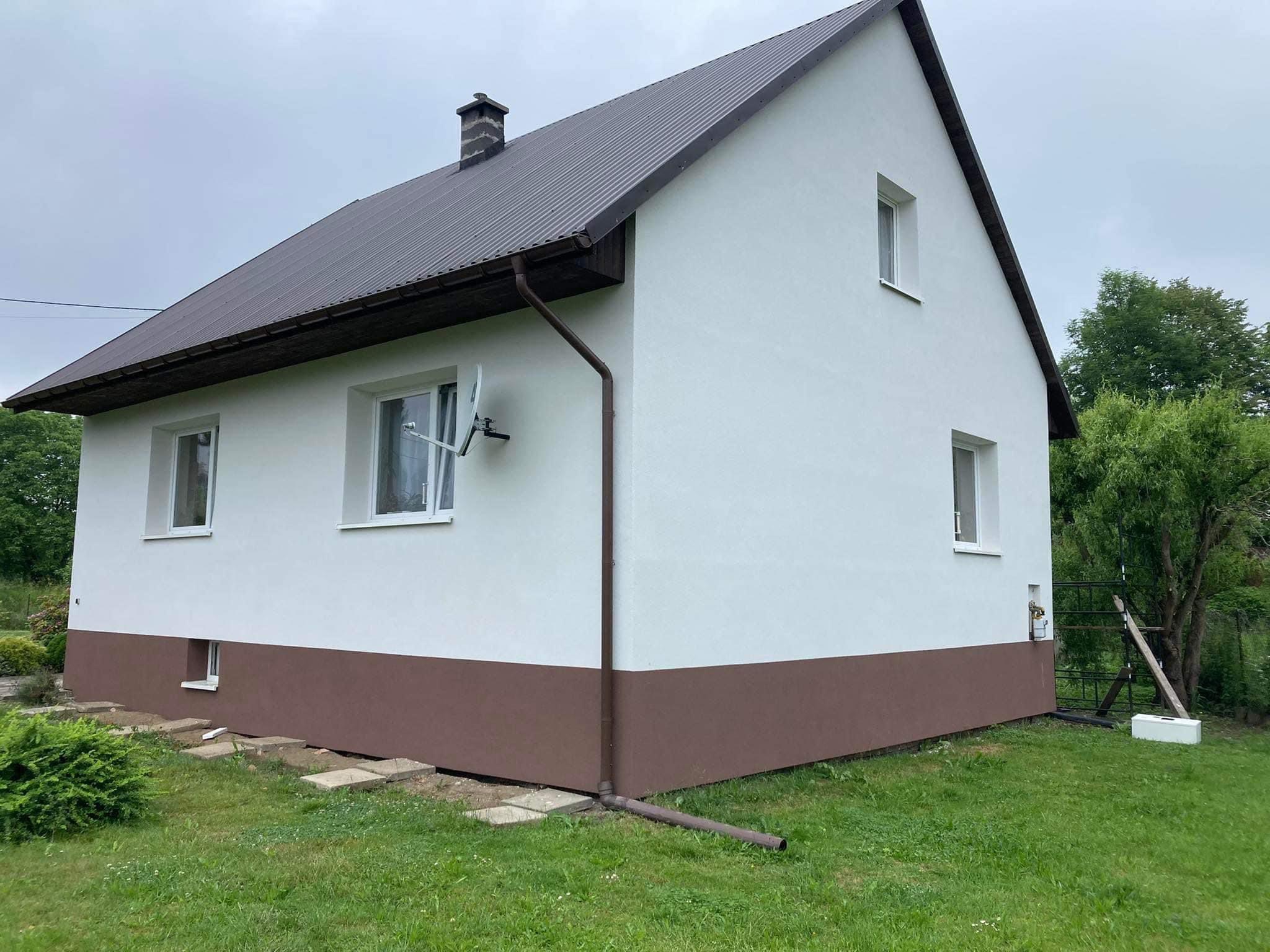 Dwukolorowy dom jednorodzinny z brązowym dachem i elewacją w kolorze białym i brązowym, antena satelitarna na ścianie, widok z zewnątrz.