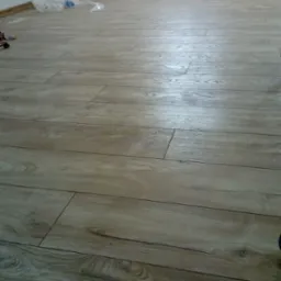 Ułożone panele podłogowe w jasnym odcieniu drewna, widoczne ślady po pracy, w tle butelka wody i folia ochronna.