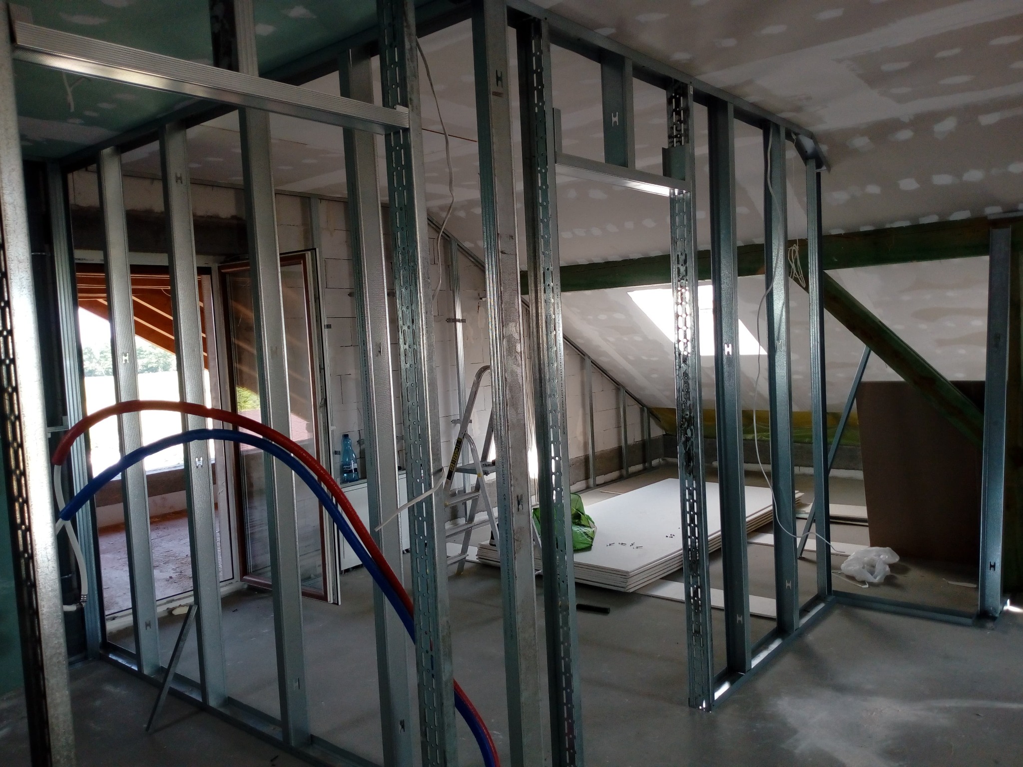 Konstrukcja szkieletowa z profili stalowych pod ścianę działową z płyt gipsowo-kartonowych w trakcie budowy, widoczne przewody instalacji wodnej, drabina i płyty g-k.