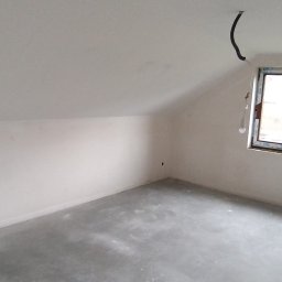 Gerbud - Poddasze po szpachlowaniu, widoczne gładkie ściany i przygotowana podłoga. Okno z PCV w prawym rogu, przewody elektryczne zwisają z sufitu.