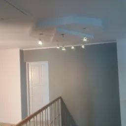 Szare ściany po malowaniu z drewnianą balustradą schodów i sześcioma lampami sufitowymi