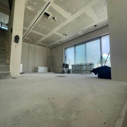 REMONT-BUD Jakub Ćwikłowski - Wnętrze w trakcie prac wykończeniowych: sufit z płyt kartonowo-gipsowych z widocznymi łączeniami, ściany przygotowane do dalszej obróbki, podłoga surowa, widoczne narzędzia i materiały budowlane...