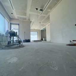 REMONT-BUD Jakub Ćwikłowski - Wnętrze w trakcie prac wykończeniowych: ściany przygotowane, częściowo wyszpachlowane, widoczna maszyna do malowania natryskowego, sufity podwieszane z płyt gipsowo-kartonowych z widocznymi...