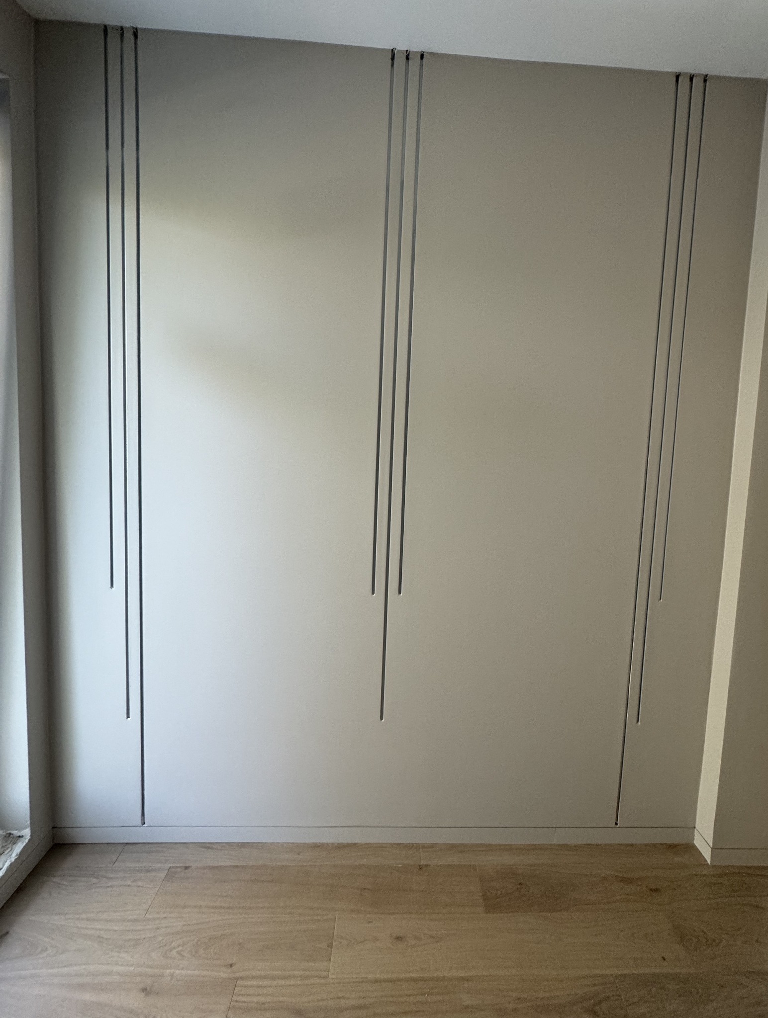 Ściana w jasnym odcieniu z dekoracyjnymi, pionowymi wcięciami, wykończona drewnopodobną podłogą.