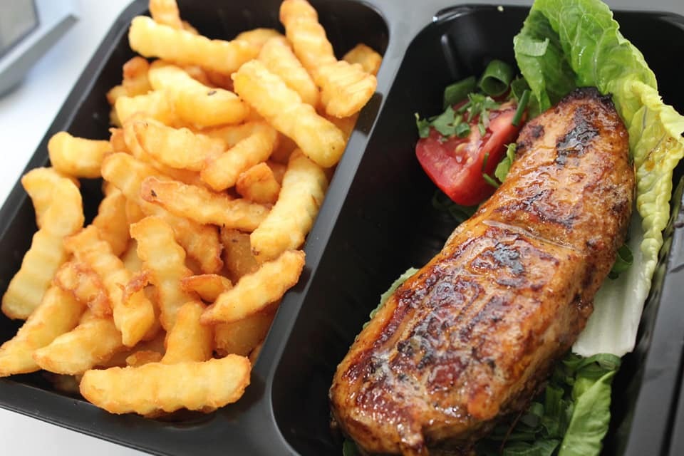 Gotowe danie w czarnym pojemniku: grillowany filet z kurczaka na sałacie z pomidorem i frytki karbowane.
