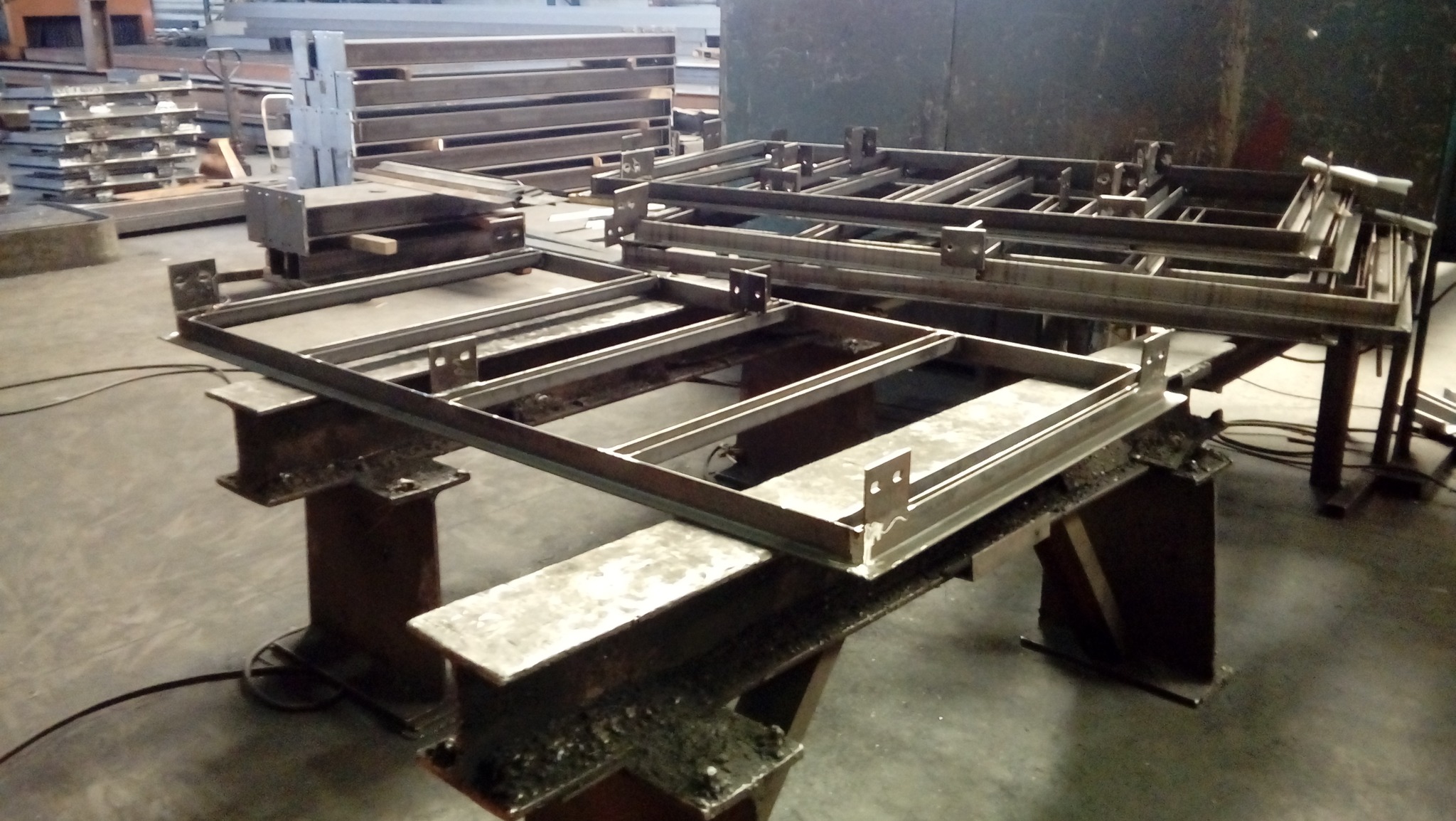 Surowe, spawane ramy z profili stalowych z mocowaniami, ułożone jedna na drugiej w hali produkcyjnej, widoczne niedoskonałości spoin.