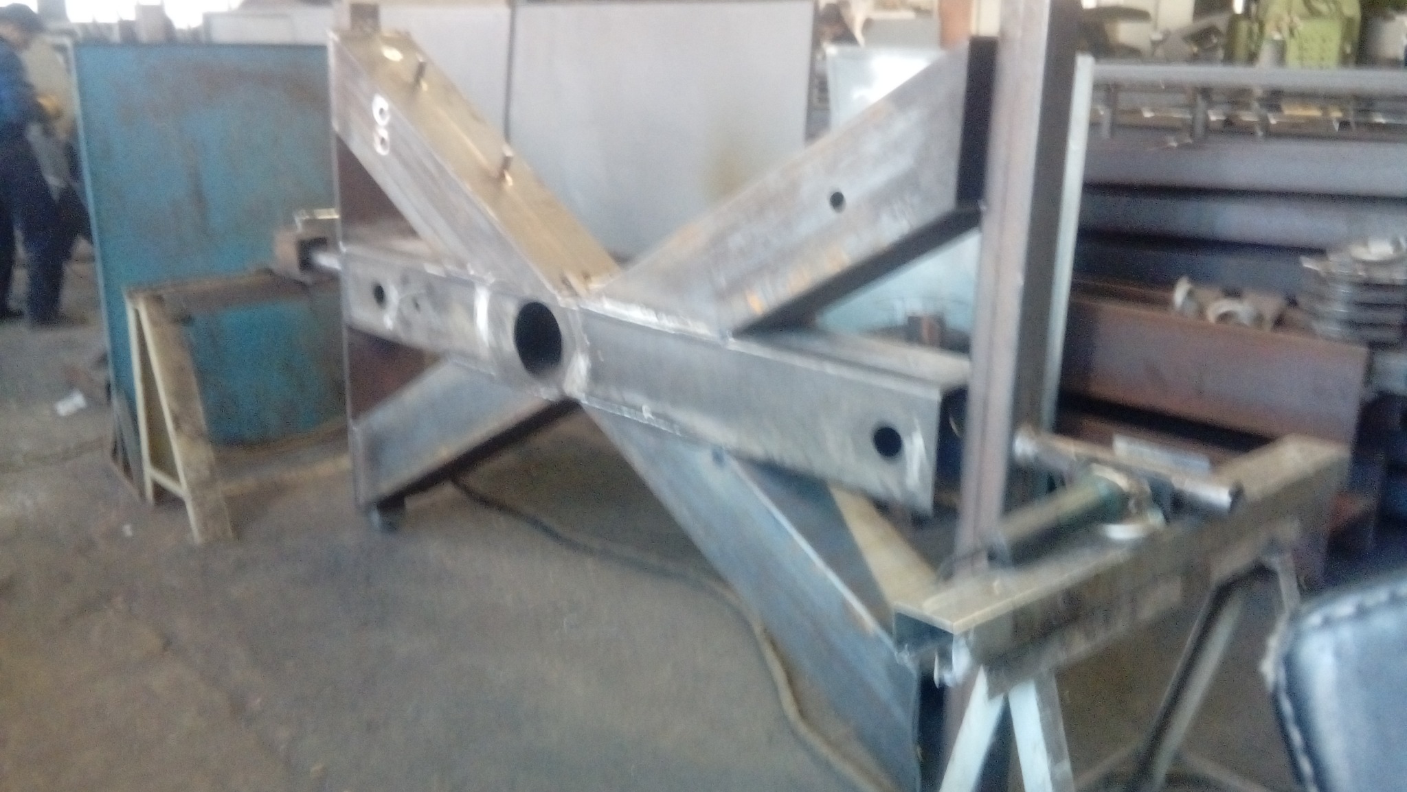 Konstrukcja stalowa w kształcie litery X z otworami, spawana z profili zamkniętych, ustawiona na kozłach w warsztacie.