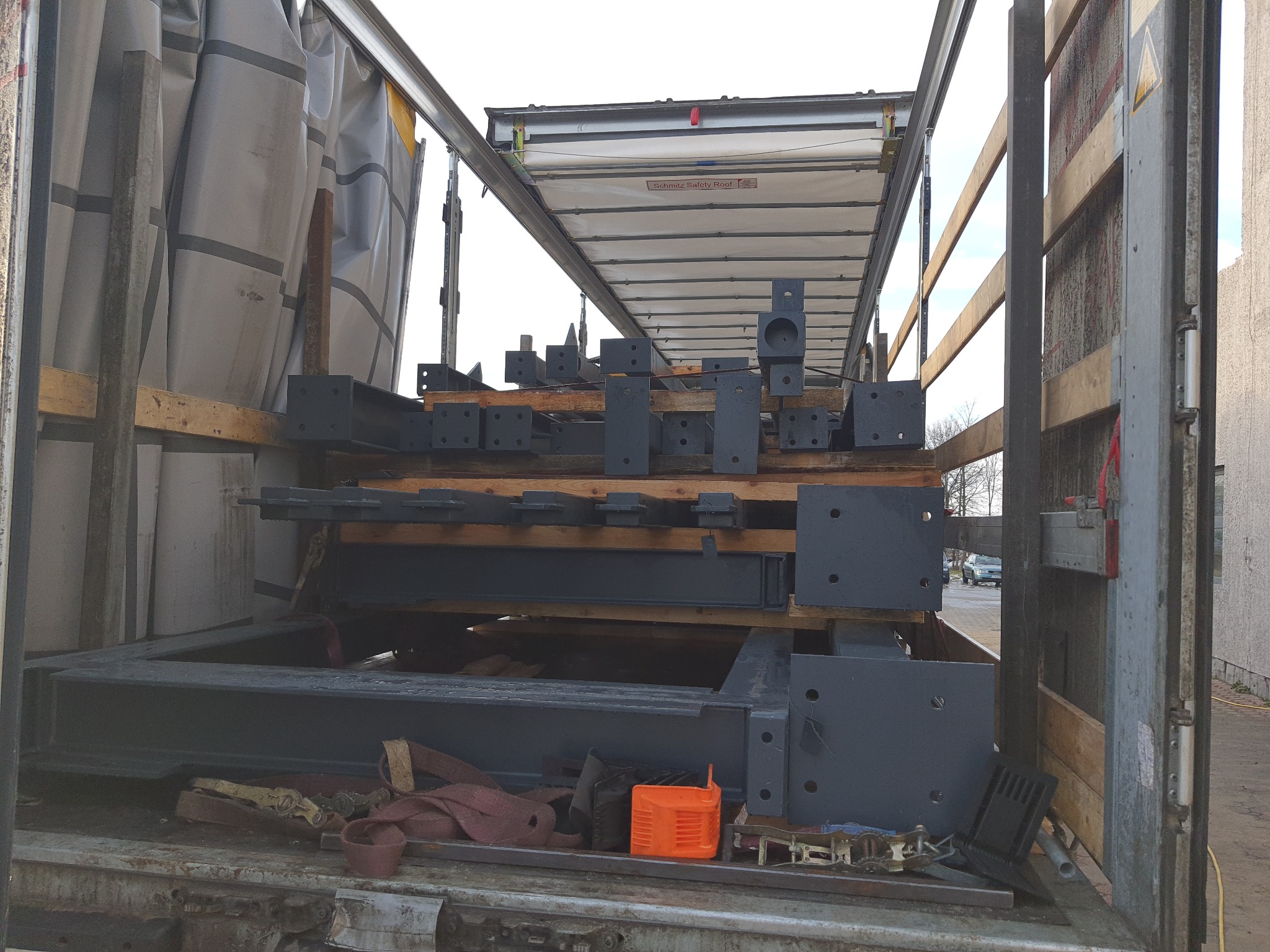 Części konstrukcji stalowej, pomalowane na szaro, zabezpieczone drewnianymi belkami wewnątrz naczepy ciężarówki podczas transportu.