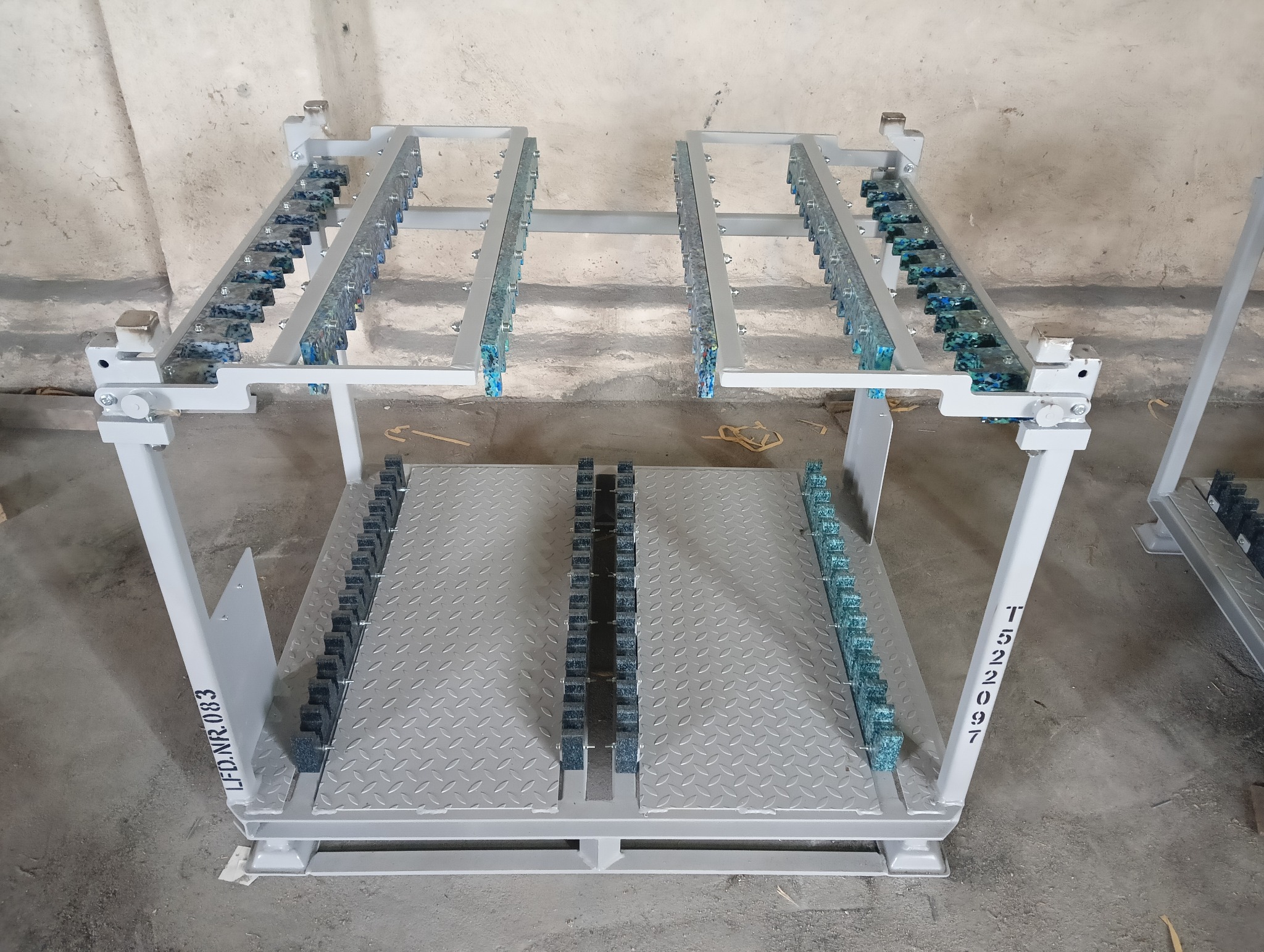 Metalowa konstrukcja w kolorze jasnoszarym, prawdopodobnie wózek do transportu elementów po procesie obróbki, z rzędami otworów na detale, widoczny numer seryjny LFD.NR.083 oraz T522097