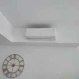 Biała klimatyzacja marki Fujitsu zamontowana na ścianie w nowoczesnym wnętrzu, obok dekoracyjny zegar z rzymskimi cyframi.