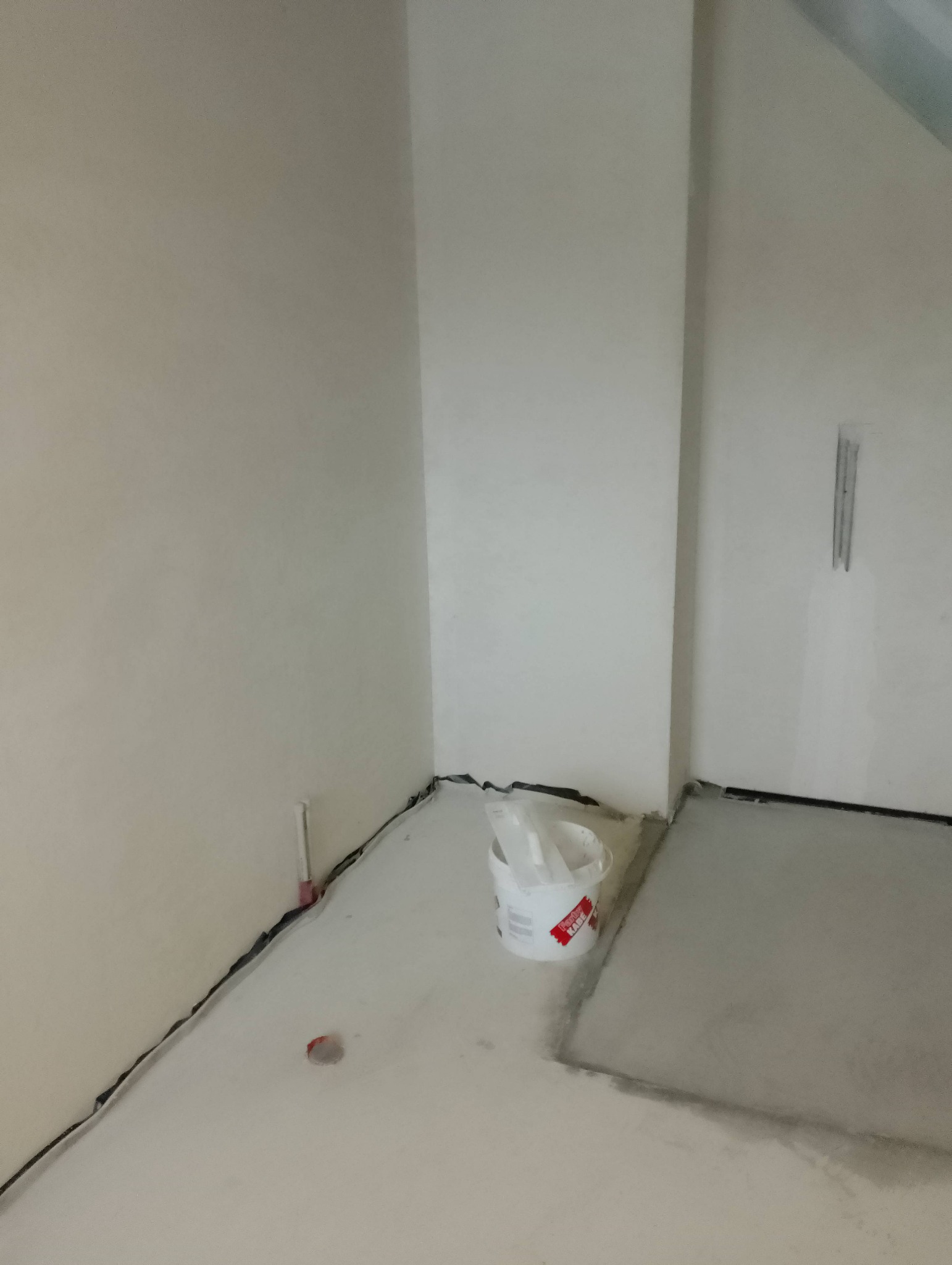 Świeżo pomalowane ściany w narożniku pomieszczenia, widoczne ślady taśmy malarskiej przy podłodze oraz wiadro z farbą marki Kabe.