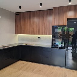 F.H.U Kamix Kamil Zieliński - Nowoczesna kuchnia z drewnianymi szafkami górnymi i czarnymi dolnymi, blatem z ciemnego kamienia i wbudowanym sprzętem AGD. Widoczne refleksy w lodówce.