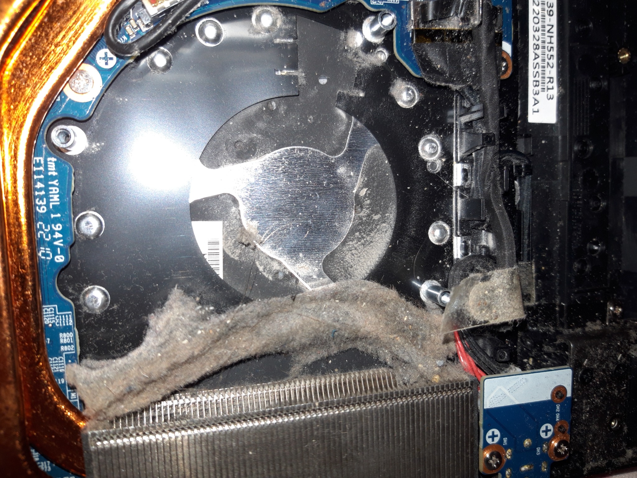 Wnętrze brudnego komputera stacjonarnego z kurzem na wentylatorze i radiatorze procesora, widoczne elementy płyty głównej i okablowanie.