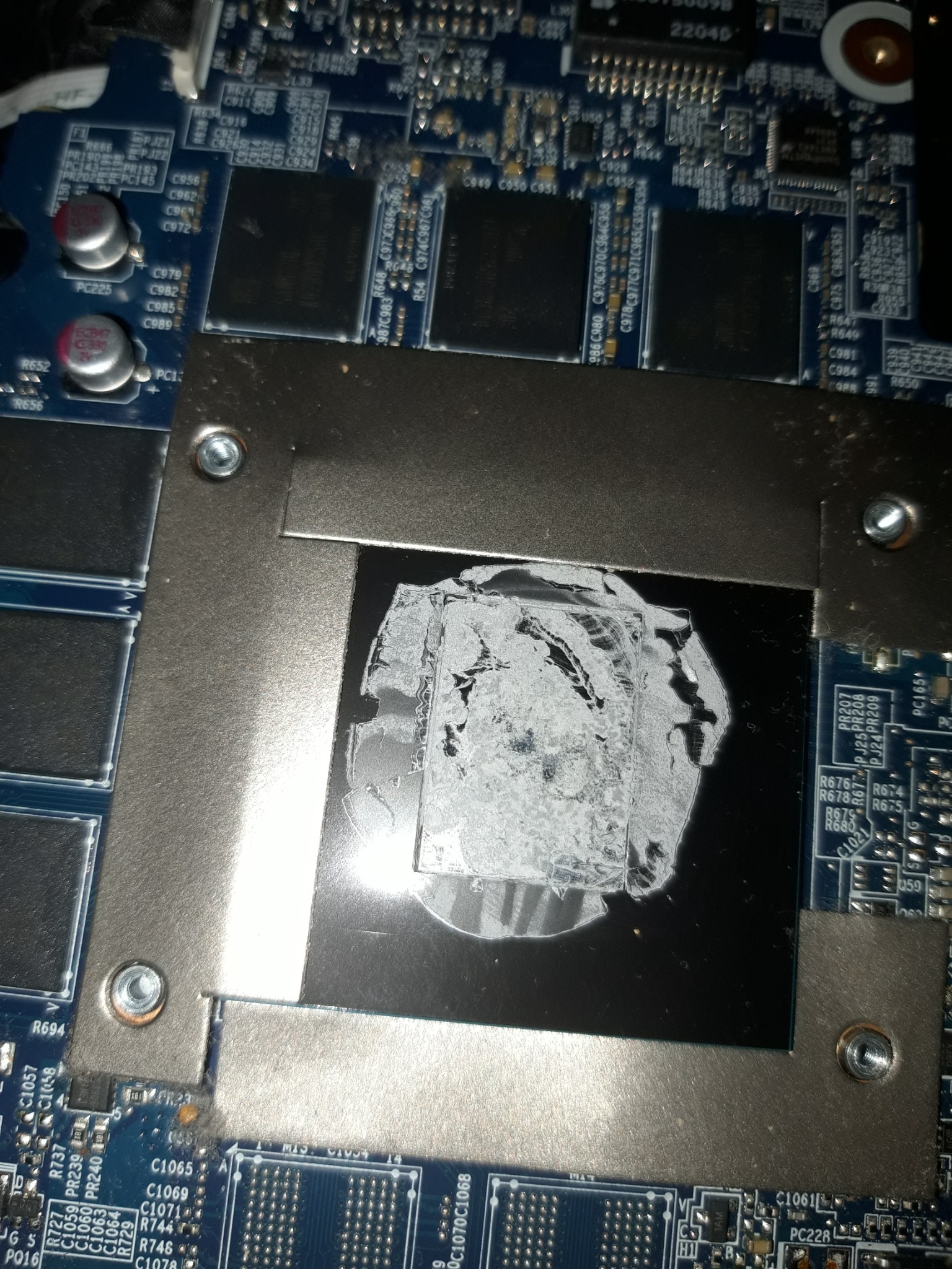 Oczyszczony procesor graficzny z resztkami pasty termoprzewodzącej, widoczny metalowy radiator i elementy płyty głównej laptopa, detale elektroniki.