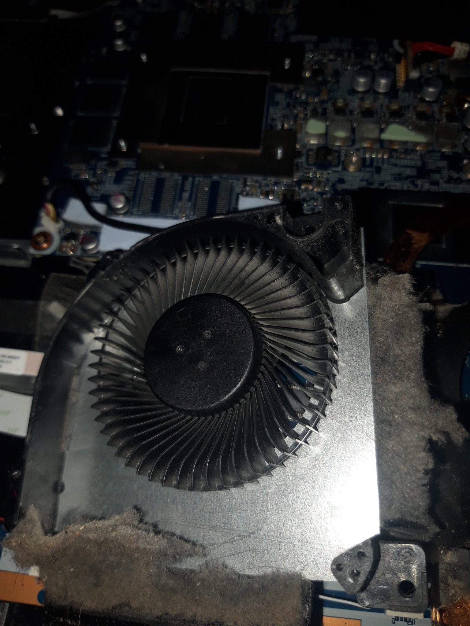 Detail of a dusty laptop fan removed from the motherboard during a repair, showing accumulated dust and debris.