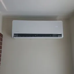 Biały klimatyzator Rotenso zamontowany na ścianie w pomieszczeniu w Zdunach, widoczny fragment ściany z cegły i okno z roletą.