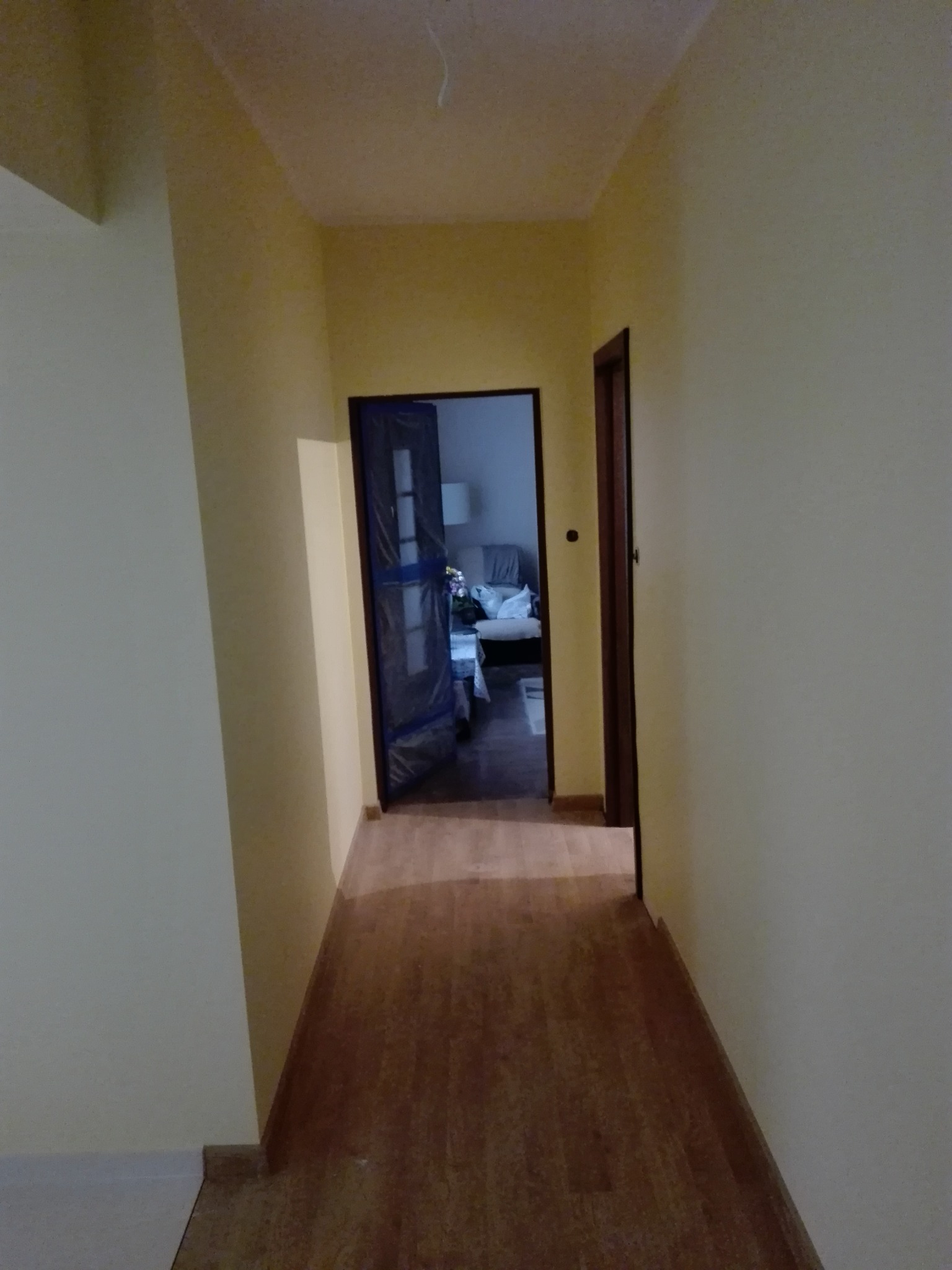 Korytarz po malowaniu ścian na odcień żółci, z widoczną drewnianą podłogą i drzwiami wejściowymi do pokoju z sofą.