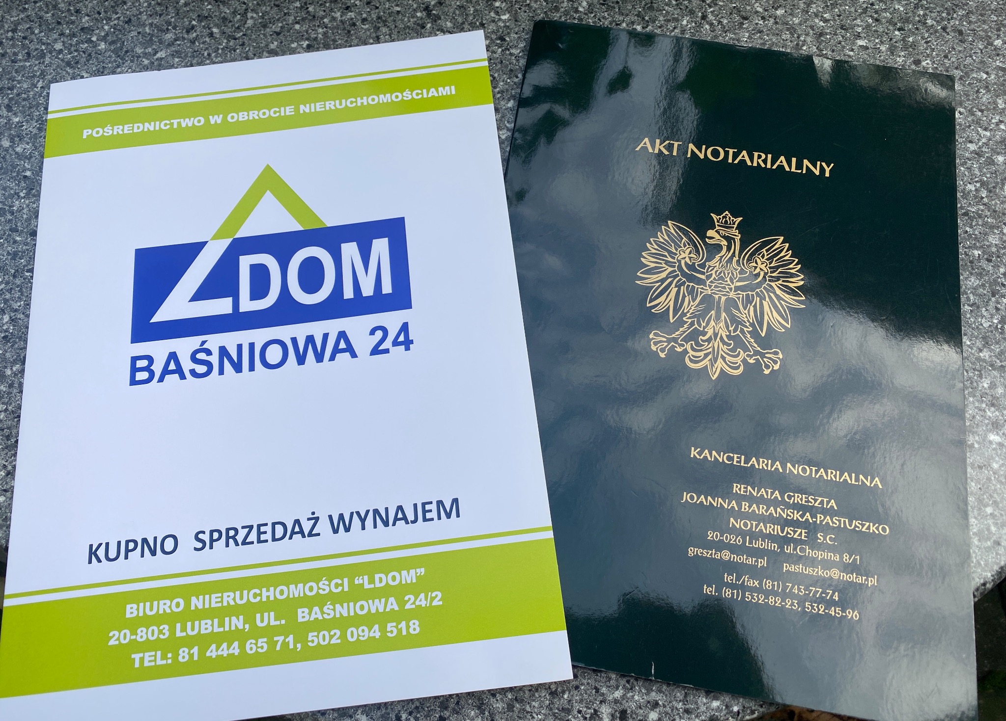 Ujęcie z góry: ulotka agencji nieruchomości LDOM z Lublina, obok niej zielony akt notarialny z godłem Polski, leżące na szarym tle.