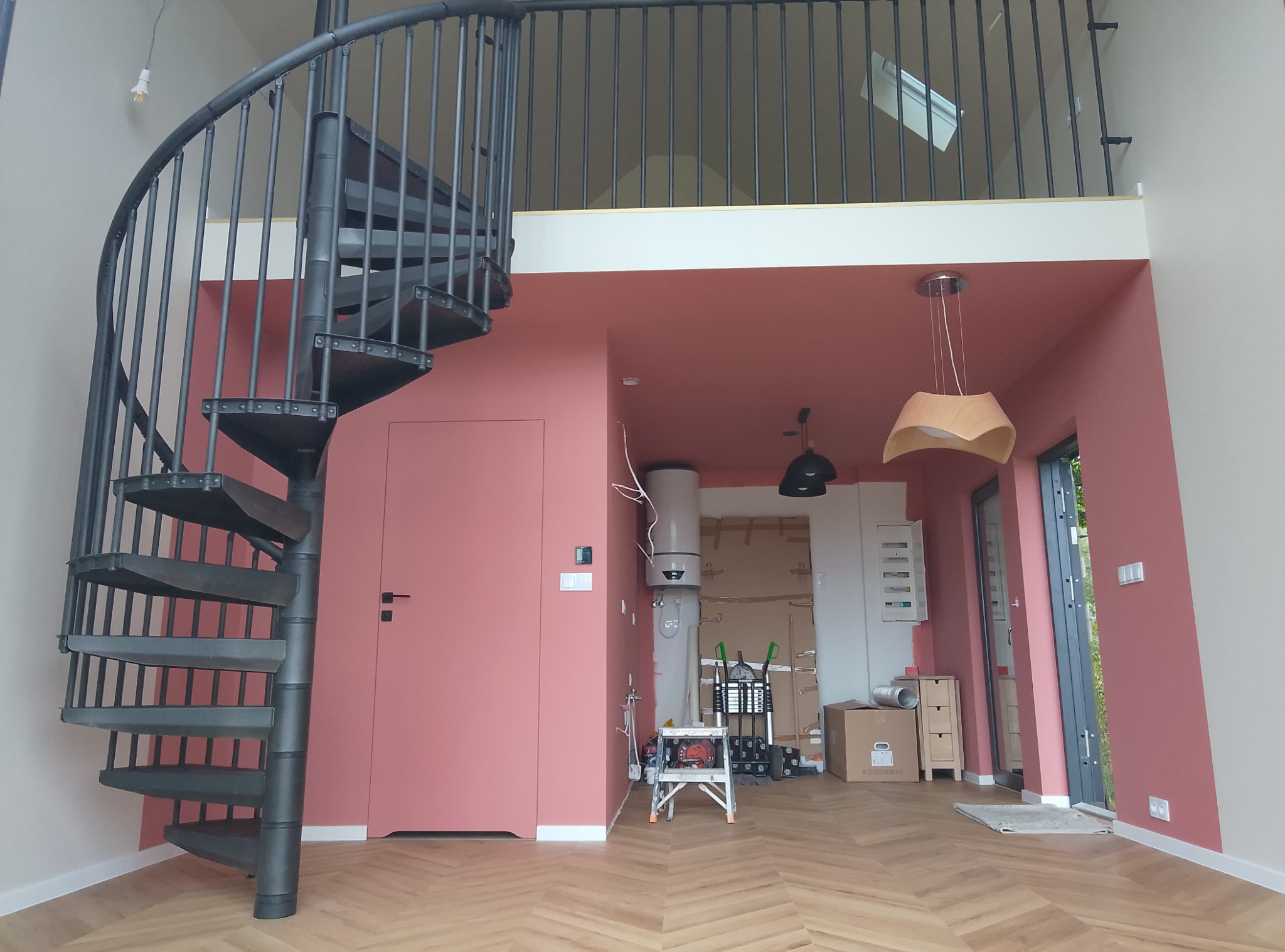Wnętrze w Złocieńcu z spiralnymi schodami, świeżo pomalowanymi ścianami w odcieniach różu, widoczne narzędzia malarskie i grzejnik, podłoga ułożona w jodełkę.