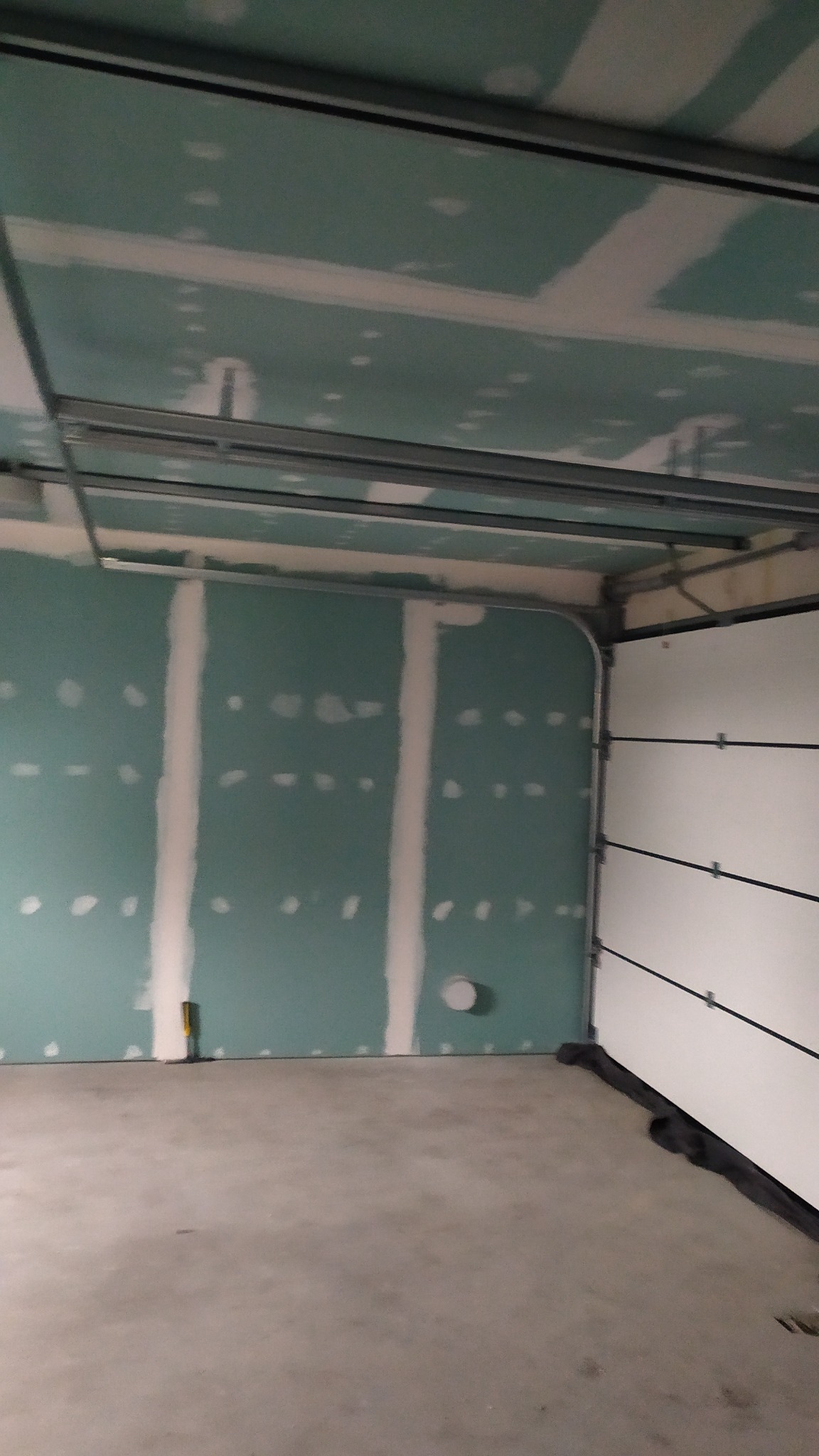 Wnętrze garażu z zamontowaną konstrukcją metalową pod sufitem i płytami kartonowo-gipsowymi na ścianach, spoiny między płytami wstępnie wypełnione szpachlą.