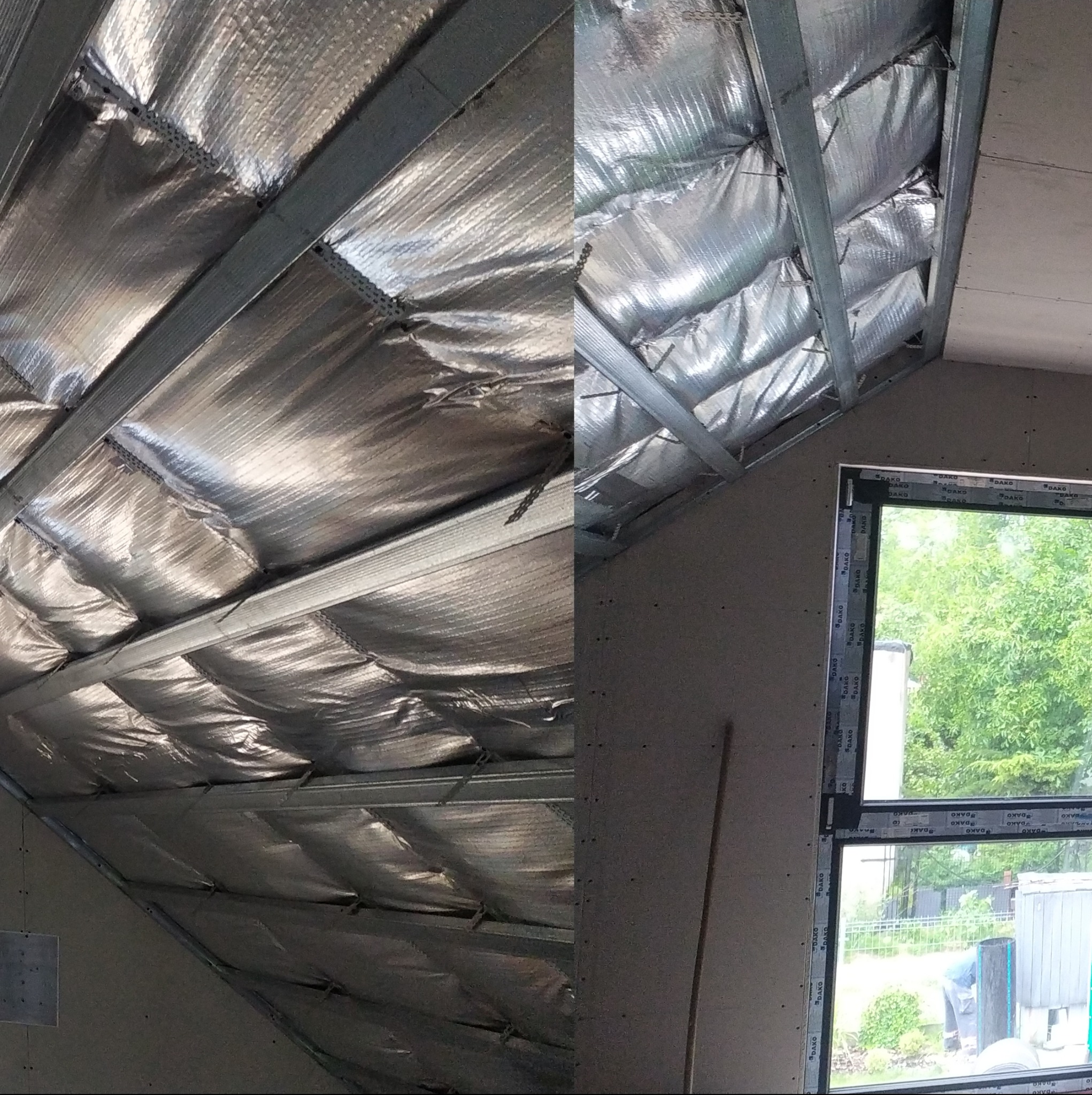 Skośny strych z izolacją termiczną pokrytą folią aluminiową, widoczne metalowe profile konstrukcyjne pod płytę karton-gips, okno z widokiem na zieleń.