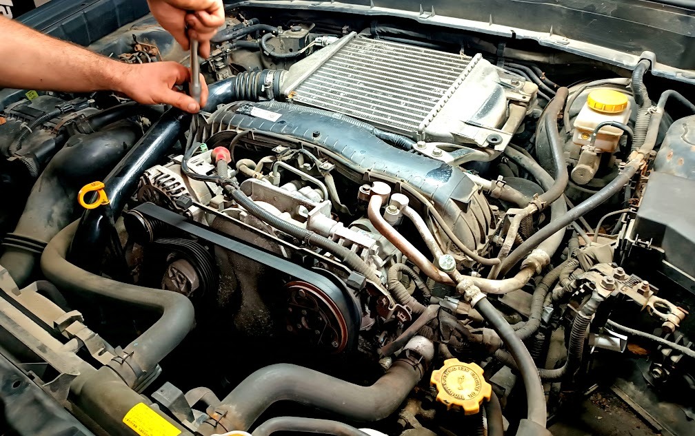 Mechanik dokręca śrubę w silniku Subaru z turbodoładowaniem, widoczny intercooler i pasek rozrządu.