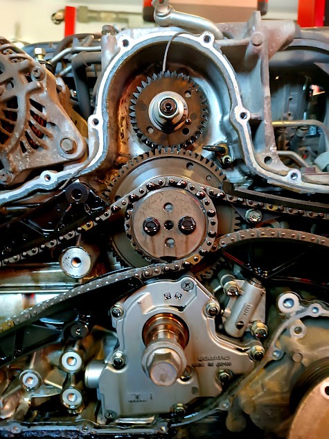 Odsłonięty silnik Subaru z widocznymi zębatkami, łańcuchem rozrządu i pompą oleju, detale mechaniczne w zbliżeniu.