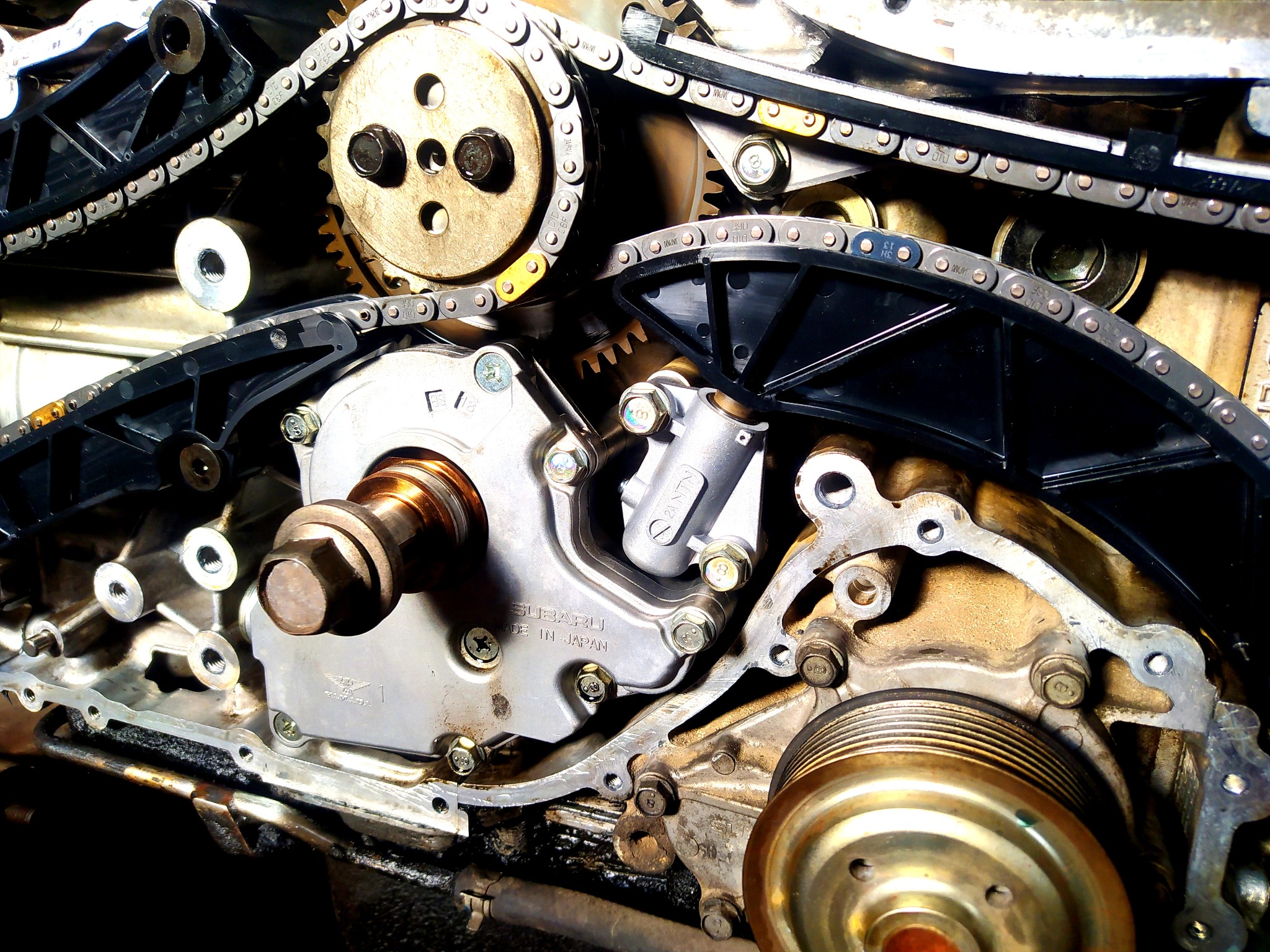 Odsłonięty silnik Subaru z łańcuchem rozrządu, kołami zębatymi i elementami montażowymi, widoczne ślady oleju.